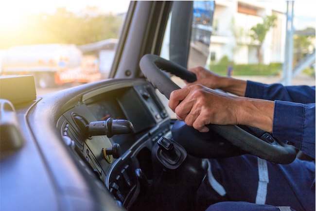 Driver holding the steering wheel inside a truck cab.