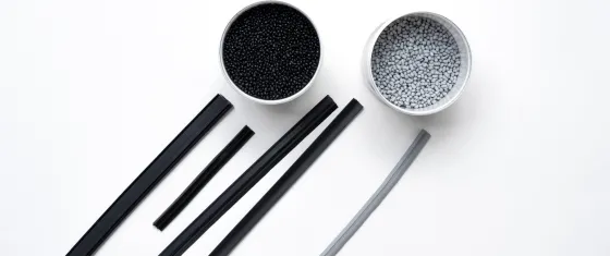 Overhead view of two small bowls—one filled with black pellets and one with light gray pellets—beside several long plastic strips in black and gray on a white background.
